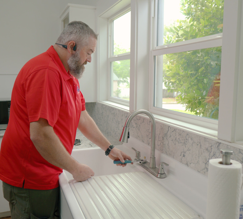A We The Plumbers plumber working at a kitchen sink