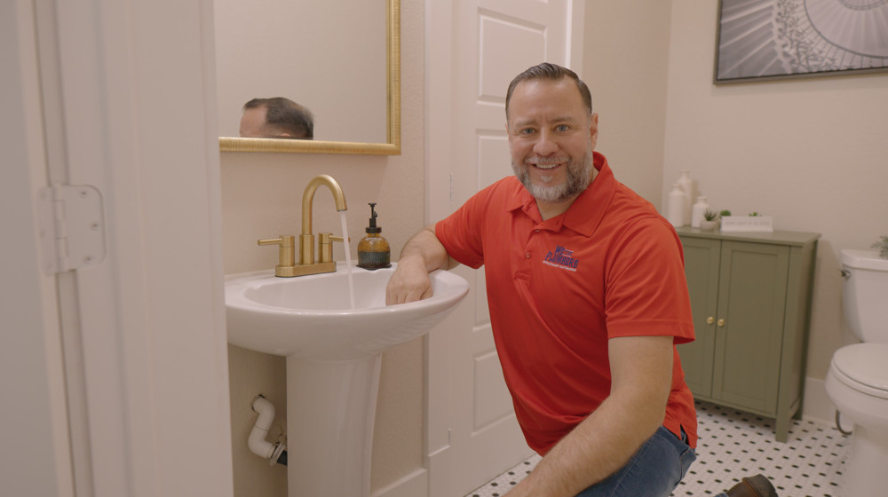 A plumber smiling beside a bathroom pedestal sink