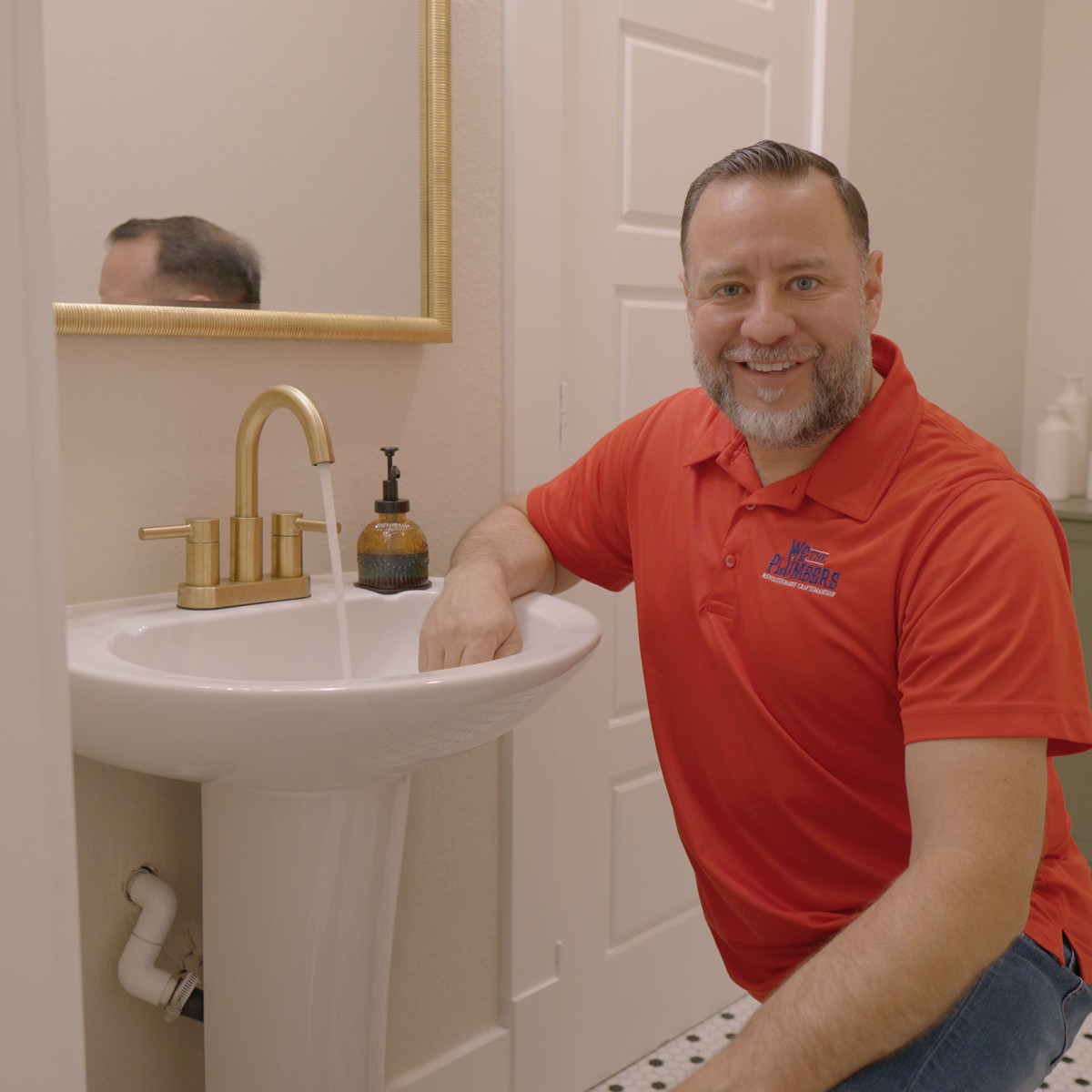 A We The Plumbers plumber smiling beside a bathroom sink